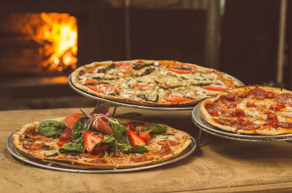 Three pizzas on display in front of a brick oven.