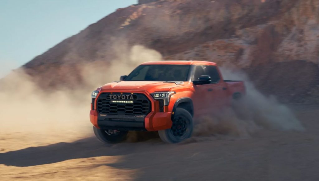 An orange 2022 Toyota Tundra driving through the dirt, desert road.