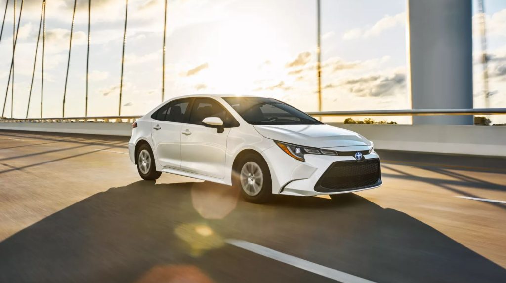 A white 2022 Toyota Corolla driving on a bridge with sun shining in the back.
