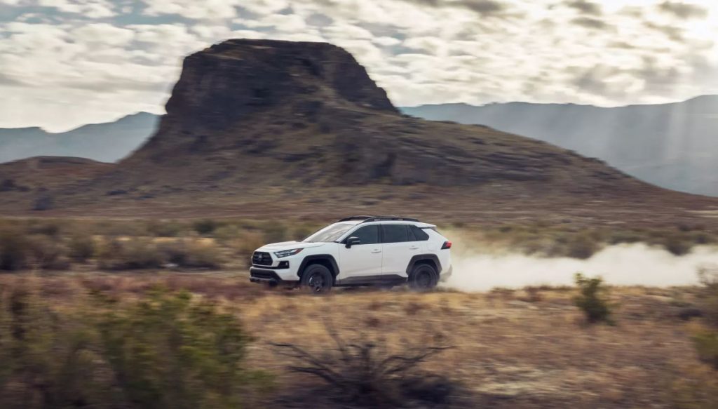 A white 2022 Toyota Rav4 driving along a desert road with smoke in its tracks. 