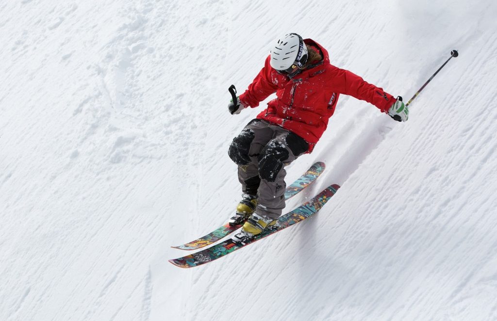 A man in a helmet and red jacket is skiing.