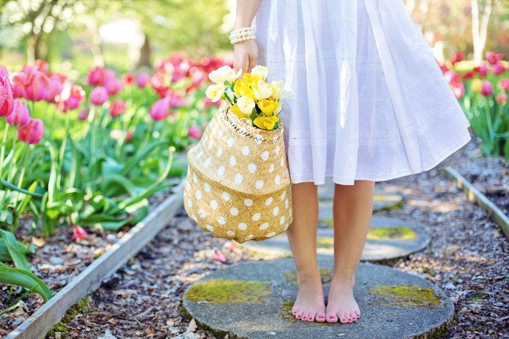 A barefoot person in a white dress holding a polka-dotted handbag with yellow tulips.