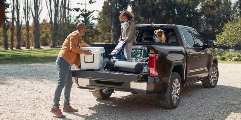A father is packing a cooler in the trunk of his 2023 Toyota Tundra. His daughter is goofing around on the trunk bed.
