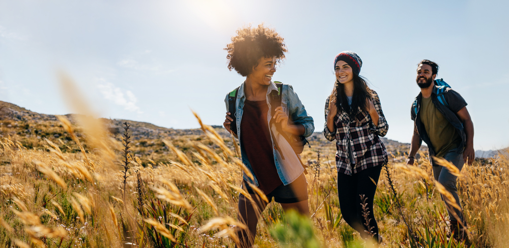 Three people hiking through a wheat field.