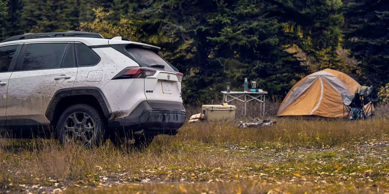 A white 2023 Toyota RAV4 parked at a campsite with a tent in the background.