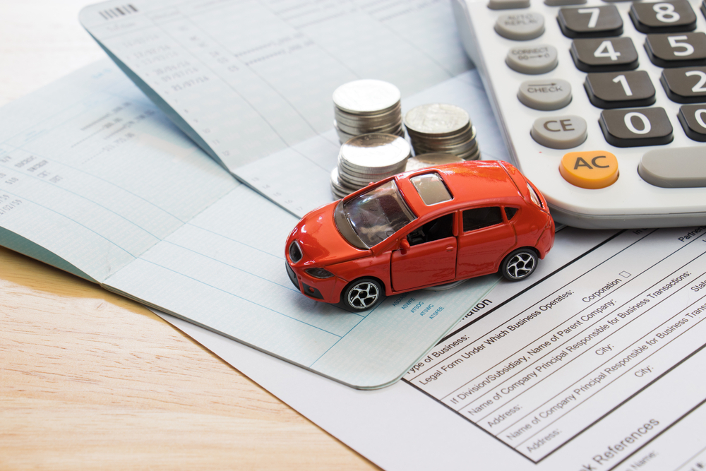 A mini car on top of financial papers with a calculator and coins stacked on the side.
